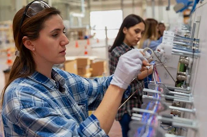 Kalfa nedir ve görevleri nelerdir? Kadın teknisyen, elektrik panosunda kablo bağlantıları yapıyor, iş ortamında dikkatli çalışıyor.