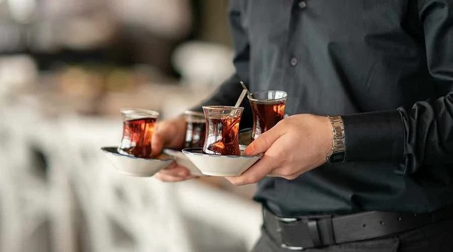 Ankara'da çay ikramı için iş ilanları Çay servis eden bir personelin elinde üç adet çay bardağı ve tabaklar yer alıyor.