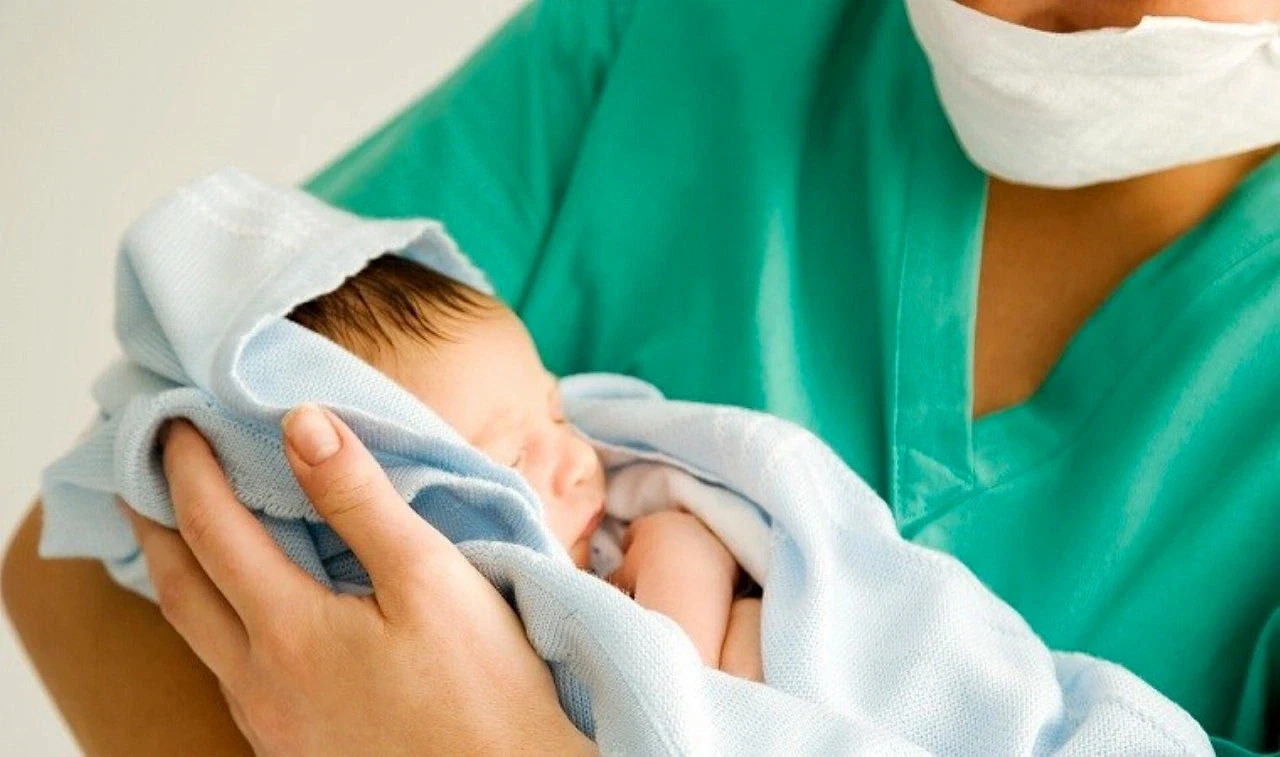 Ebelik taban puanları ve başarı sıralamaları 2026 Yeni doğmuş bir bebek, hemşire tarafından nazikçe tutuluyor.