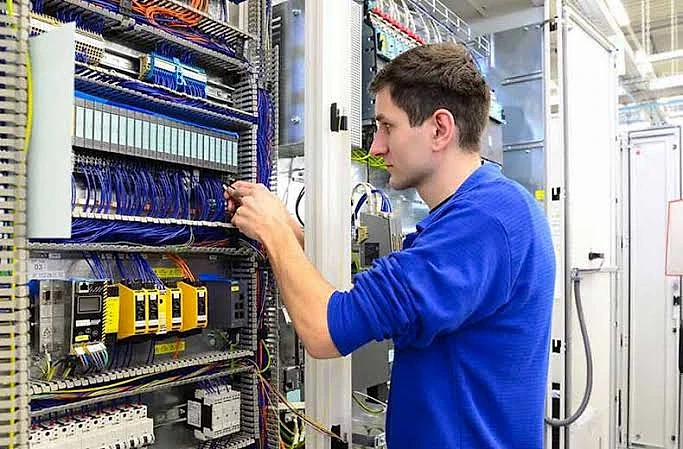 PLC programcılığı hakkında 2026 kariyer rehberi PLC programcısı, kontrol panelindeki kabloları düzenleyerek otomasyon sistemleri üzerinde çalışıyor.