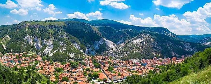 Doğal güzellikler ve köy yaşamı üzerine bir rehber Yeşil dağlarla çevrili bir köy manzarası, mavi gökyüzü ve beyaz bulutlar.