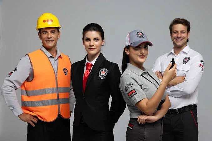 Güvenlik iş ilanları ve başvuru rehberi Farklı güvenlik görevlisi kıyafetleri giymiş dört kişi, profesyonel bir ortamda duruyor.