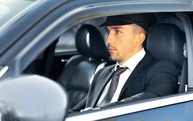Lüks araçlarda profesyonel şoför hizmeti Şık giyimli bir şoför, lüks bir araçta direksiyon başında oturuyor.